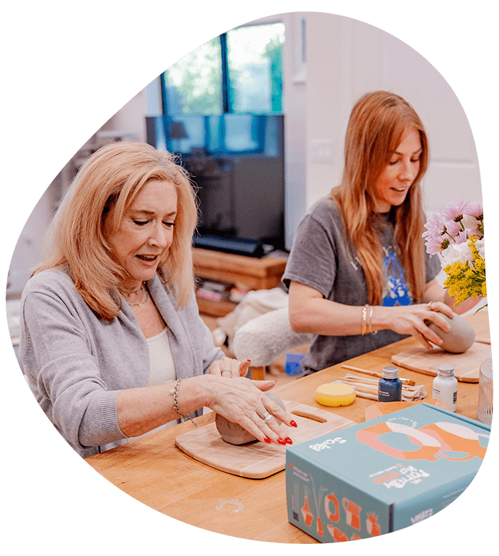 A mother and daughter share a joyful moment, hand-crafting clay pieces together in a warm space