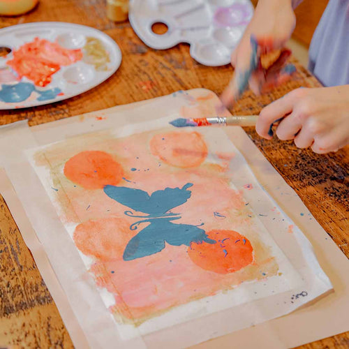 Child's hands splattering paint with a wooden brush on a Sculpd Kids Painting Kit Butterfly Stenciled on paper
