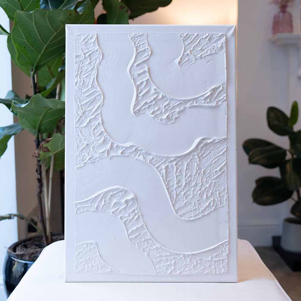 A white textured artwork stands on display with greenery in the background made using Sculpd Textured Canvas Kit
