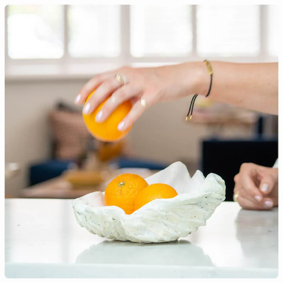 Hand placing an orange into a handmade, textured clay bowl made using Sculpd Pottery Kit filled with oranges 

